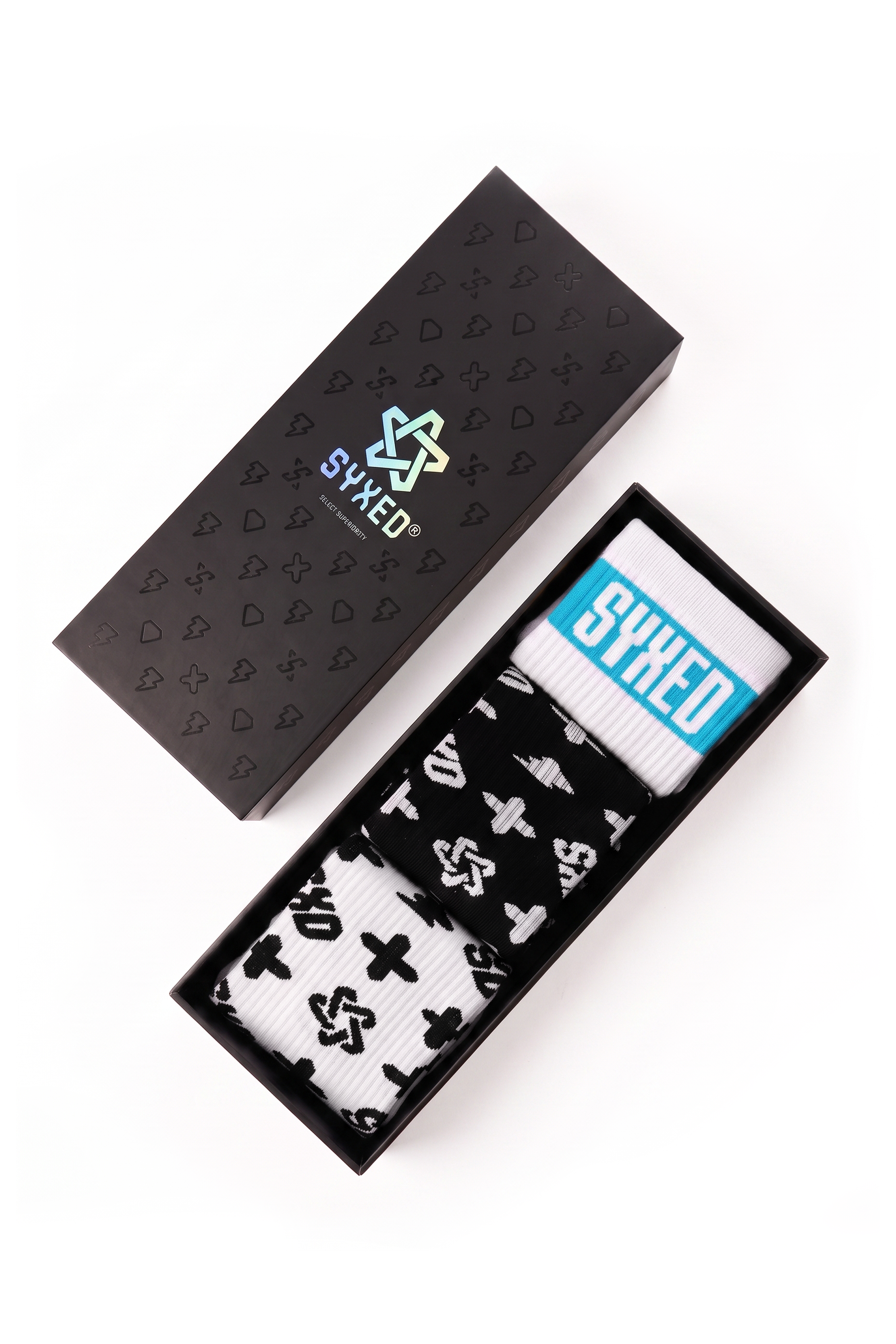 A pair of white socks with black graphic symbols and a blue 'SYXED' label, presented in an open black box next to its closed lid on a white background.