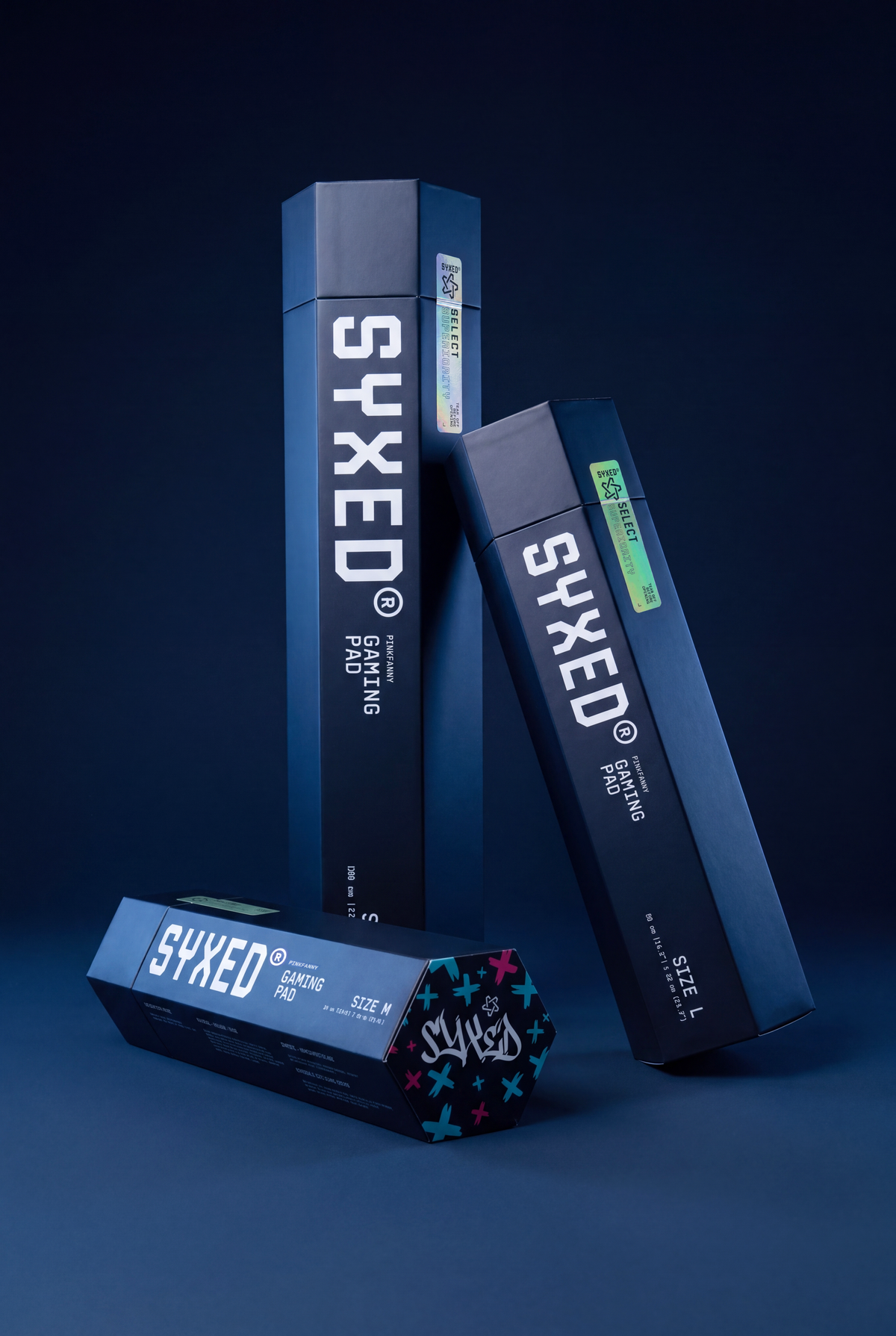 Three dark blue and black SYXED product boxes arranged on a dark blue studio background, with large white SYXED branding and smaller product text visible on the packaging.