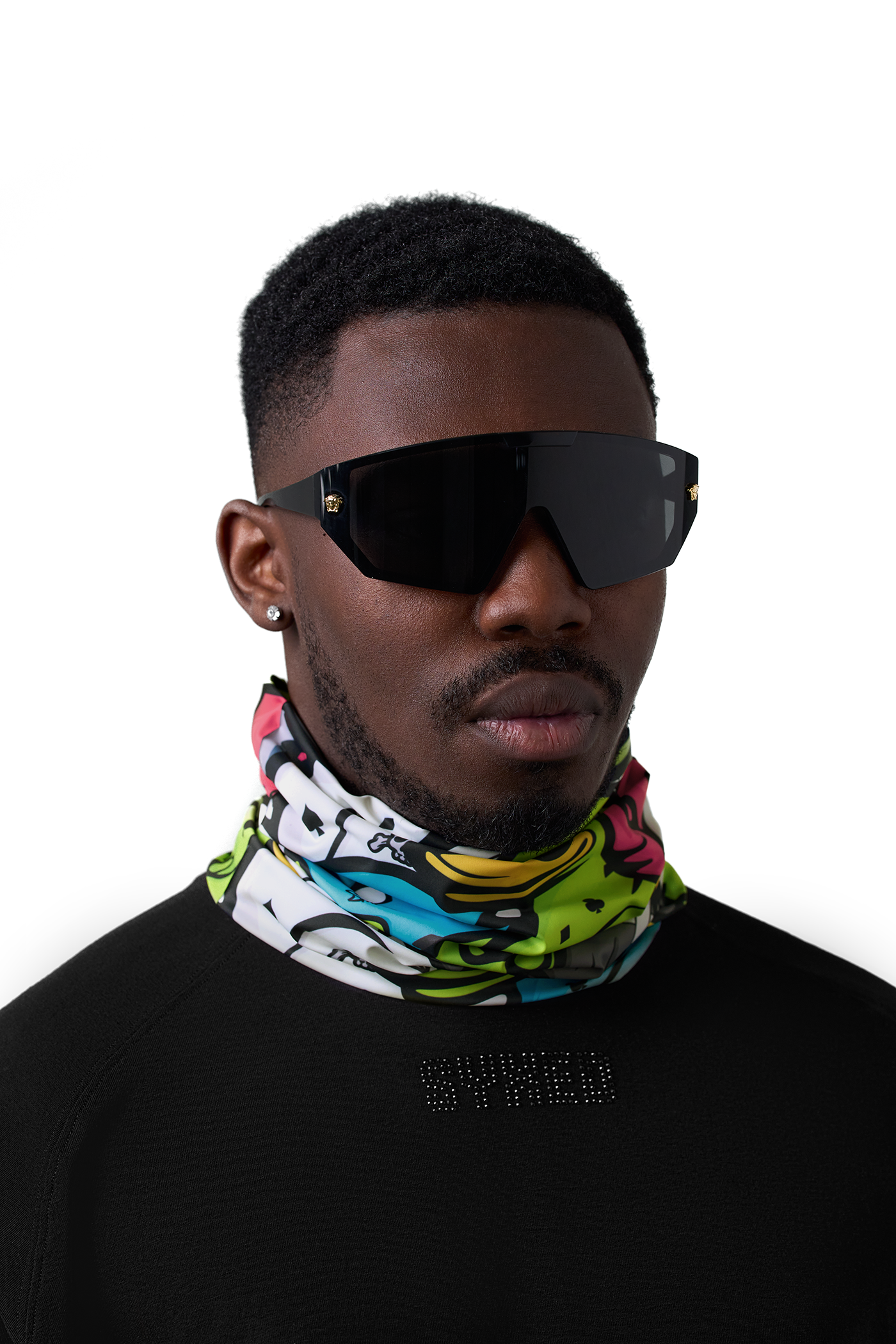 A man wearing a vibrant, multicolored graffiti-print neck gaiter and black shield sunglasses, photographed against a solid white background.