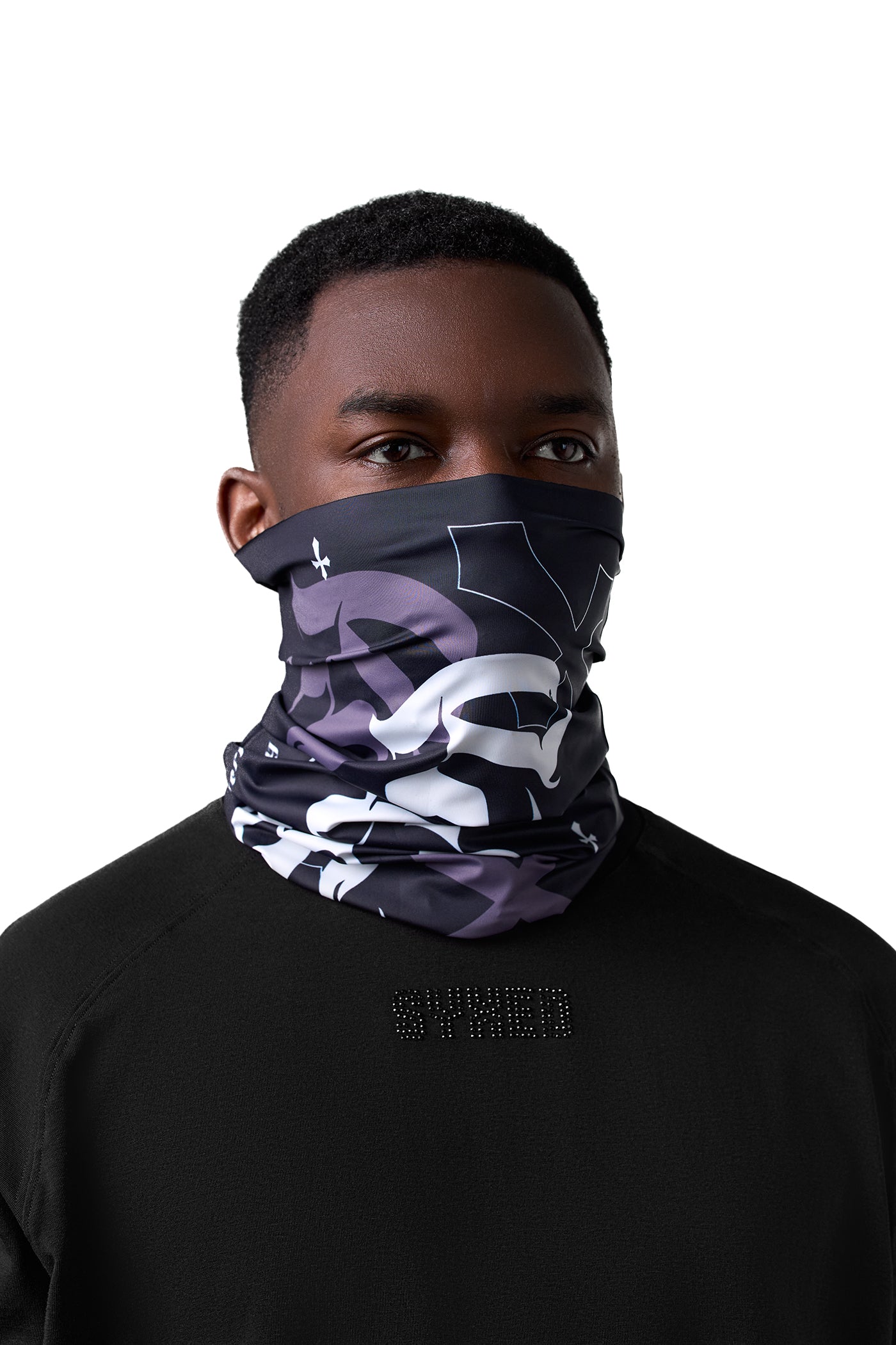 A man wearing a black, gray, and white camouflage neck gaiter mask, shown from the chest up against a solid white background.