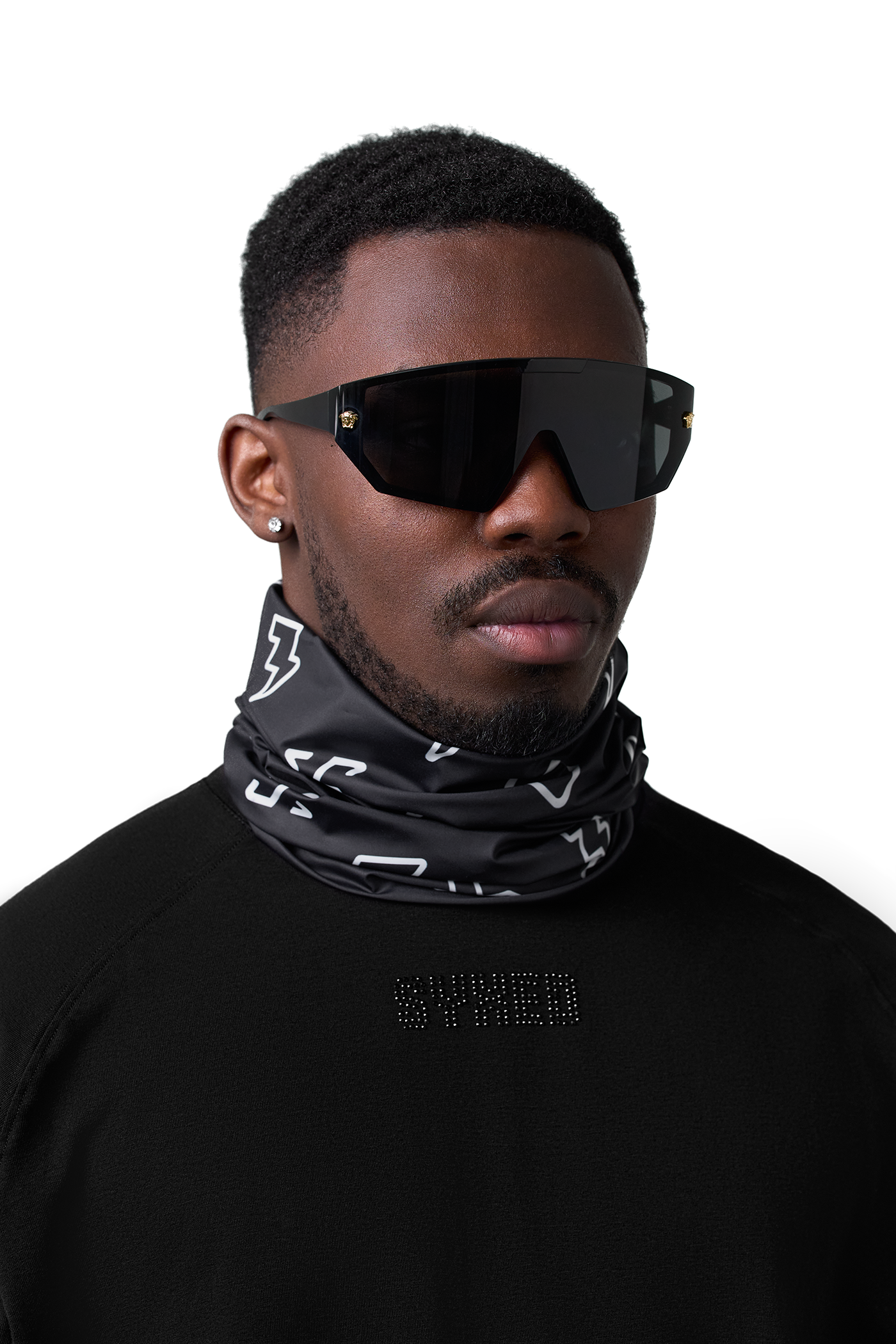 A man wearing a black and white patterned neck gaiter and black shield-style sunglasses, photographed against a plain white background.