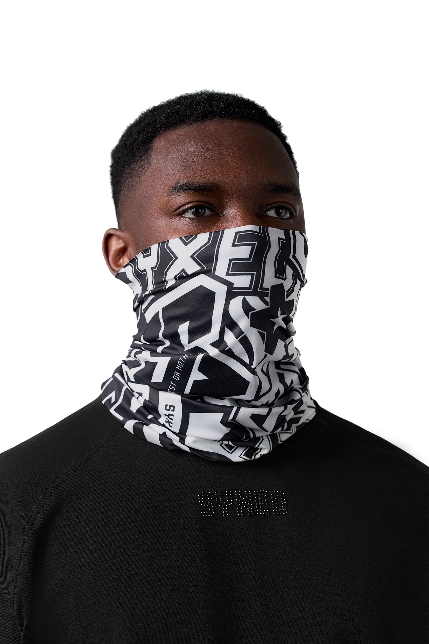 A man wearing a black and white geometric patterned neck gaiter or face mask, paired with a black crewneck sweatshirt, against a solid white background.