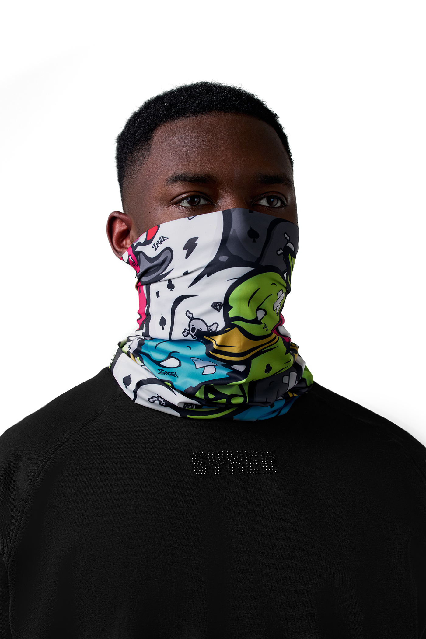 A man wearing a black crewneck sweatshirt and a white neck gaiter with a colorful cartoon graphic print, set against a plain white background.