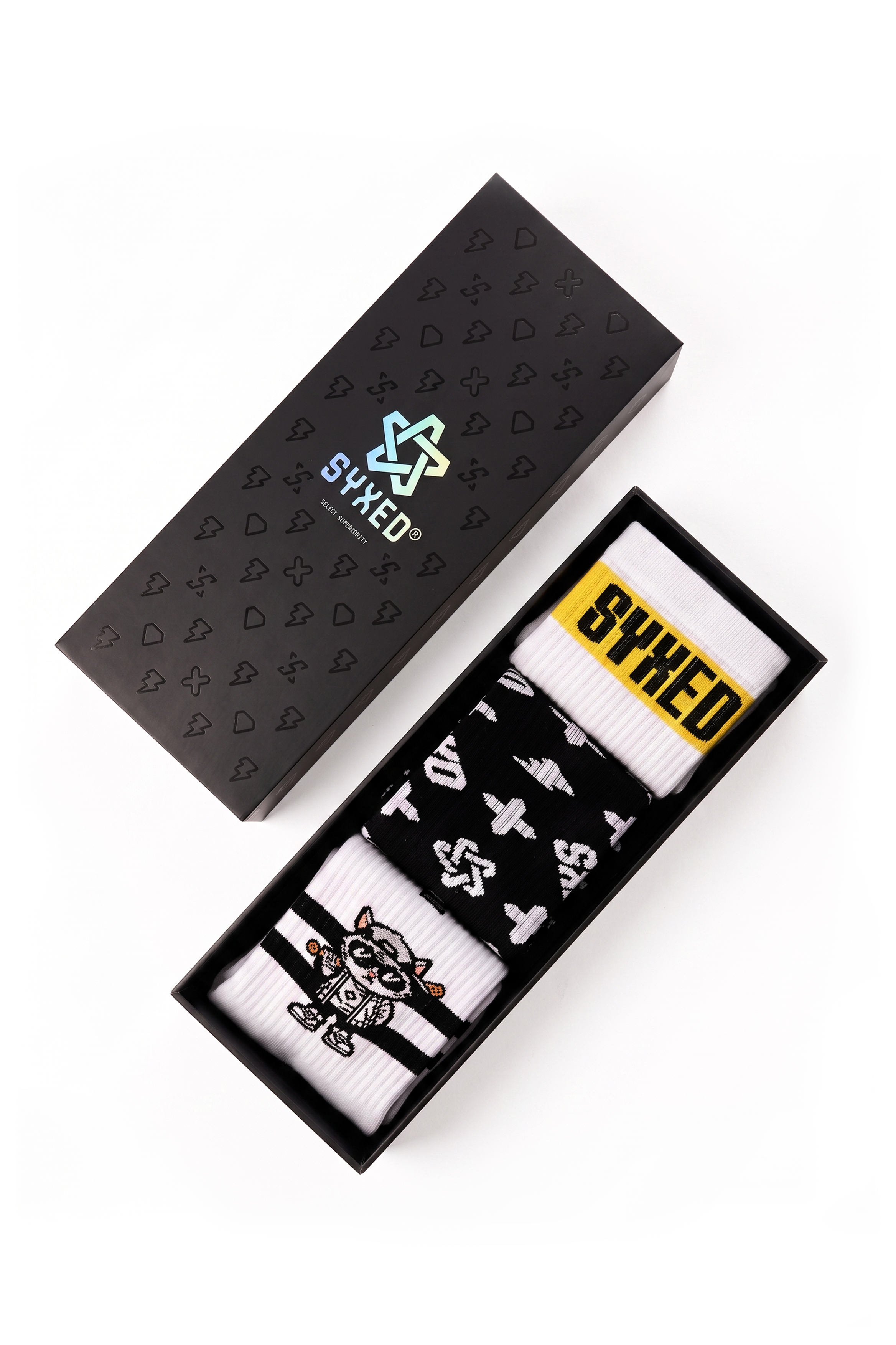 A boxed pair of patterned socks displayed on a white background, with the black presentation box lid shown above and the open box below. The socks are white and black with graphic symbols and a yellow 'SYXED' label.
