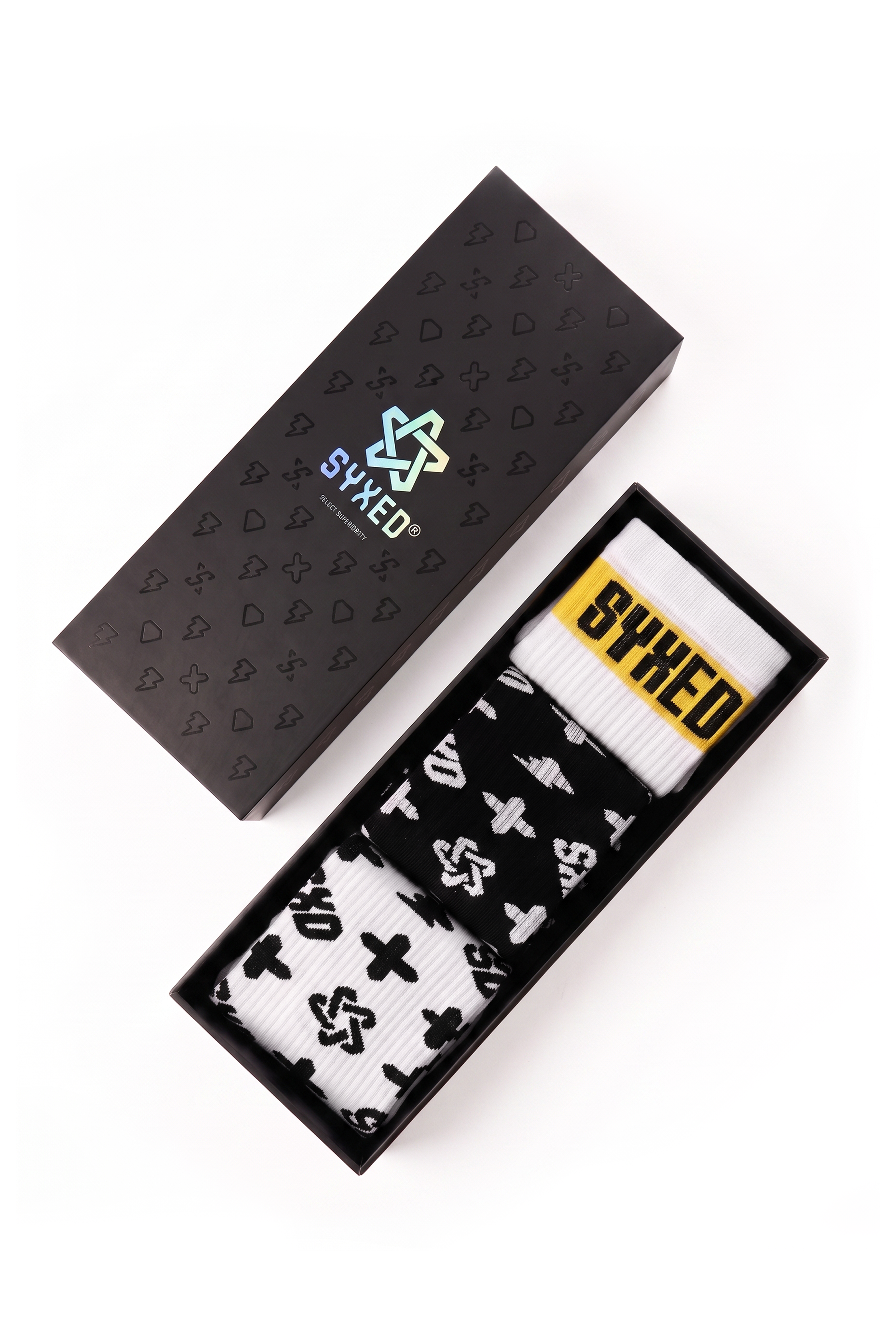 A pair of white socks with black graphic symbols and a yellow SYXED label, presented in an open black box next to its patterned black lid on a white background.
