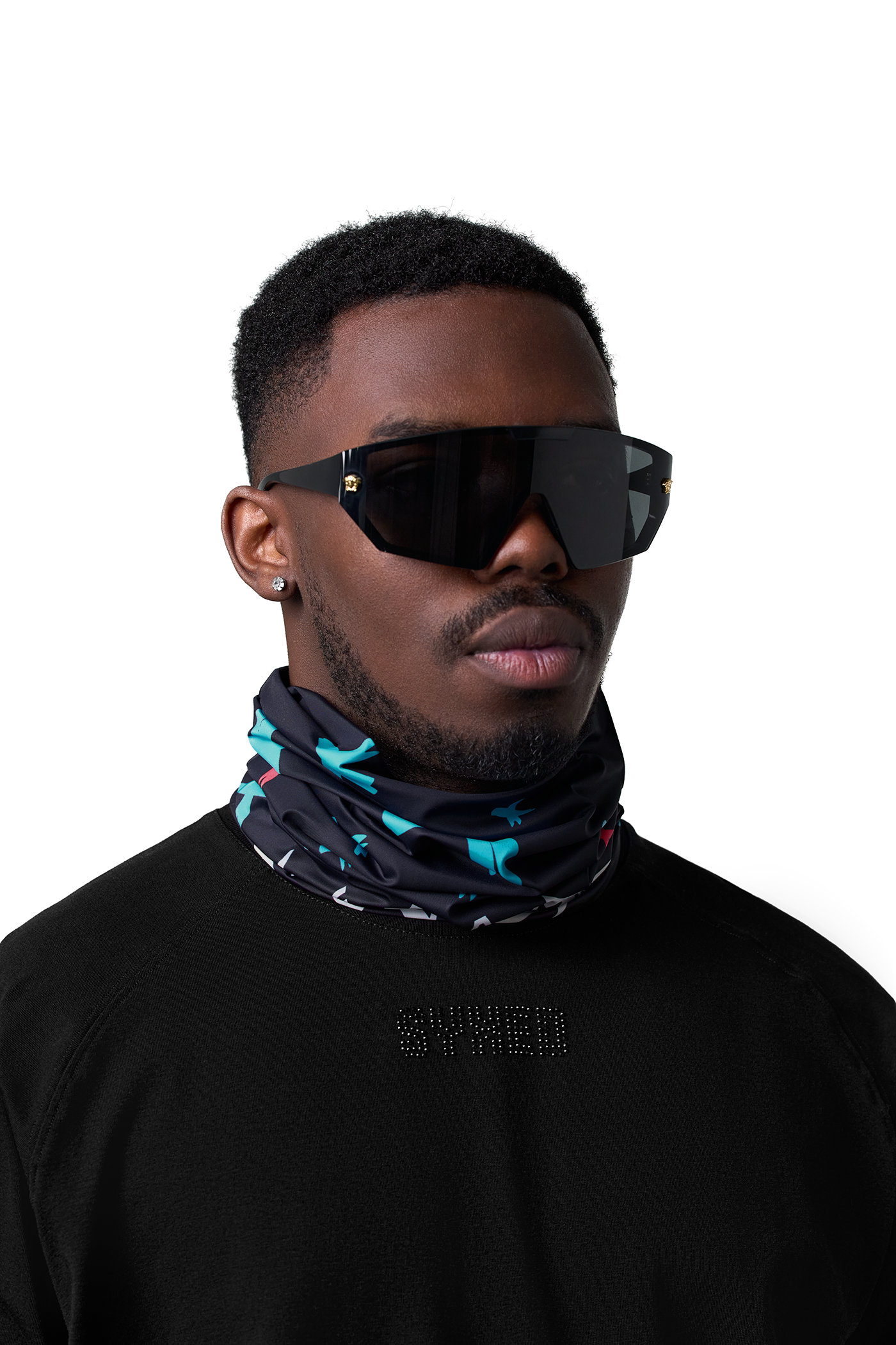 A man wearing a black and blue patterned neck gaiter and black shield-style sunglasses, photographed against a plain white background.