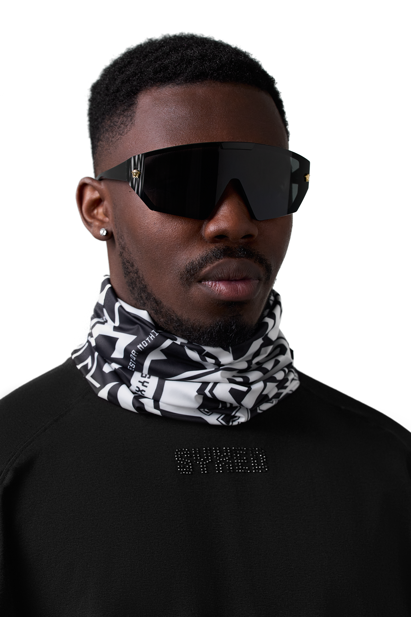 A man wearing a black and white patterned neck gaiter and black shield-style sunglasses, photographed against a plain white background.